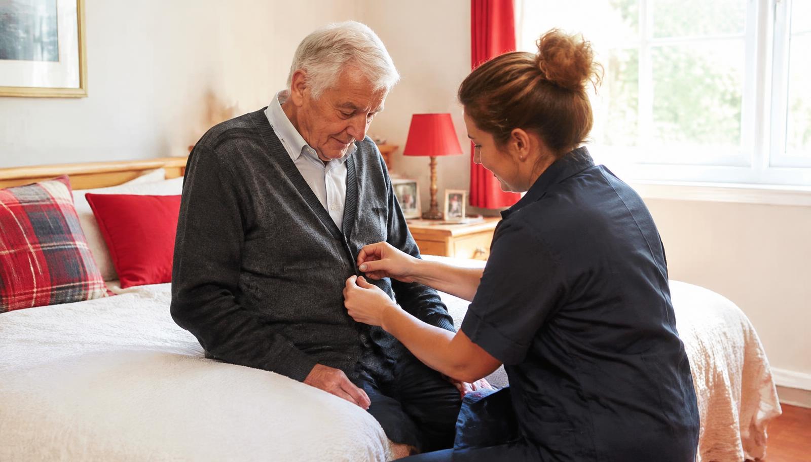 Caregiver helping a senior man button his cardigan